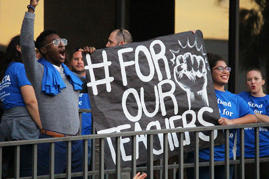 Taking a stand in favor of teacher benefits, a group of protestors hold up a sign in support of educators.
