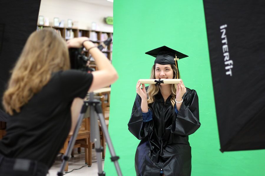 Posing for the camera, senior Emily Atkinson holds onto a prop for graduation portraits in the media center Friday Aug. 17.  The photo company will be on campus Sept. 11 and Sept. 28 to take pictures of the rest of the seniors. 