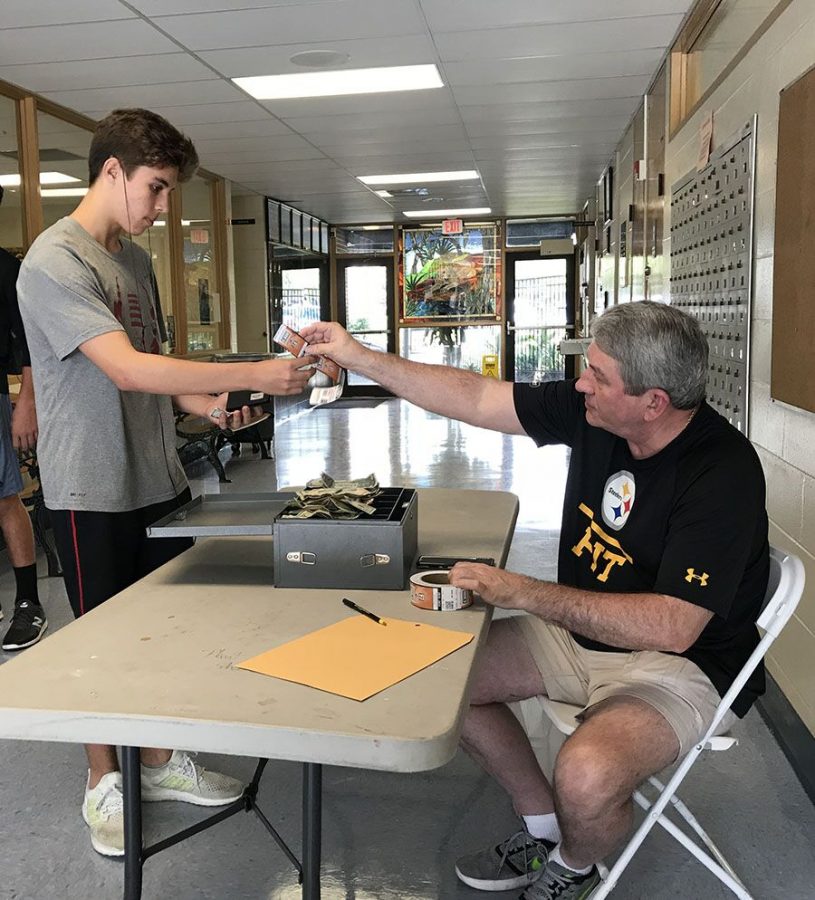 Buying tickets ahead of time, sophomore Sebastian Sargeant is greeted by retired U.S. History teacher Robert Angert, who is in charge of the ticket table in the office. Tickets will be on sale for $5 before the game at 7:30 p.m Friday, Sept. 7. 