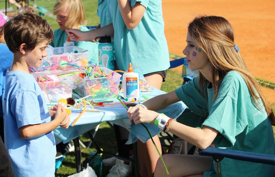 Aiding a boy with a craft, junior Ellie Schifino glues together a pipe cleaner turtle on the baseball field Friday, March 15. Spring Fling allowed interest clubs to teach young kids about their missions. 