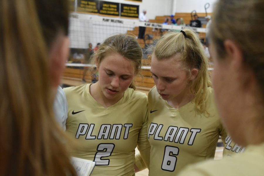Huddled with the volleyball team, sophomore Lily Frierson and senior Birdie Frierson listen to their coach at a time-out at the Alonso game Sept. 12 in the gym. The sisters began playing volleyball after watching their two older sisters enjoy the sport, too.