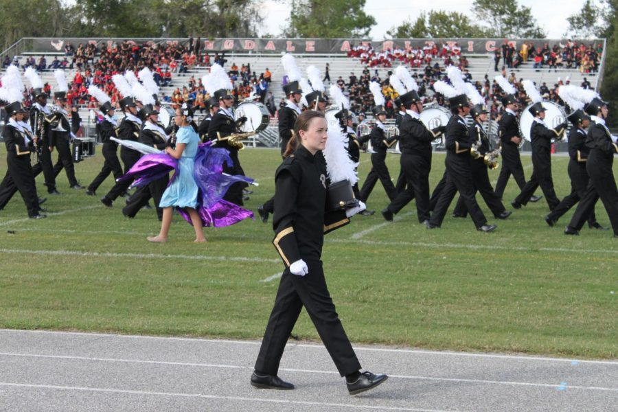 Shako in hand, drum major junior Ainsley Neil walks on the track. The drum majors use stands so the band members can see them keep time and conduct. 