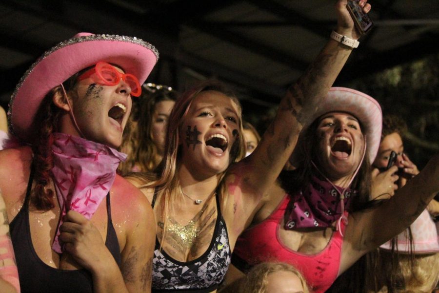 With their hands in the air seniors Katie Samel, Emma Welch and Carolee Jones cheer on the varsity football team in the second quarter. The girls wore pink paint and accessories in honor of breast cancer awareness month. 