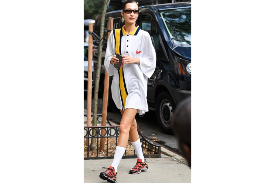 Bella Hadid wearing an oversized Nike polo shirt while strolling through New York. She finished the look with orange, black laced sneakers and black rectangular sunglasses. Her shirt is practically a dress on her, and she looks very comfortable.
