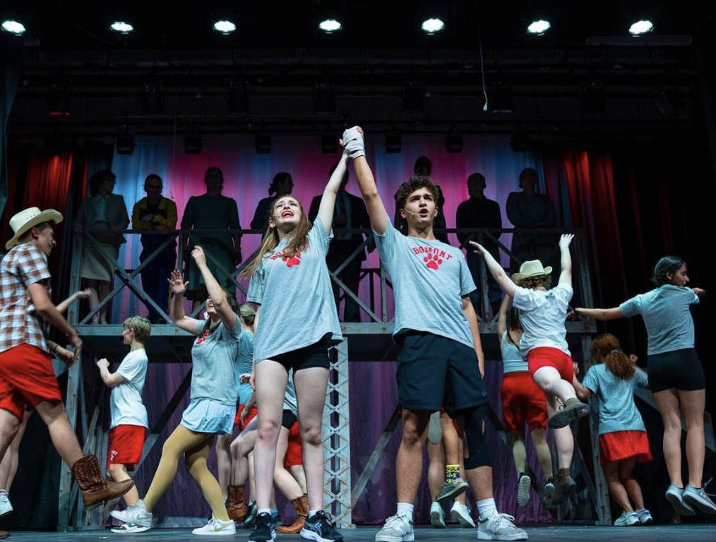 Caption: Leading stars, Ben Avriett and Eve Anton, hold their hand up high in celebration during one of the most crucial scenes in the show. Other characters dance around them as the students make the decision to rebel against the towns no dancing law.  

Picture Credits: @Benavriett on Instagram   