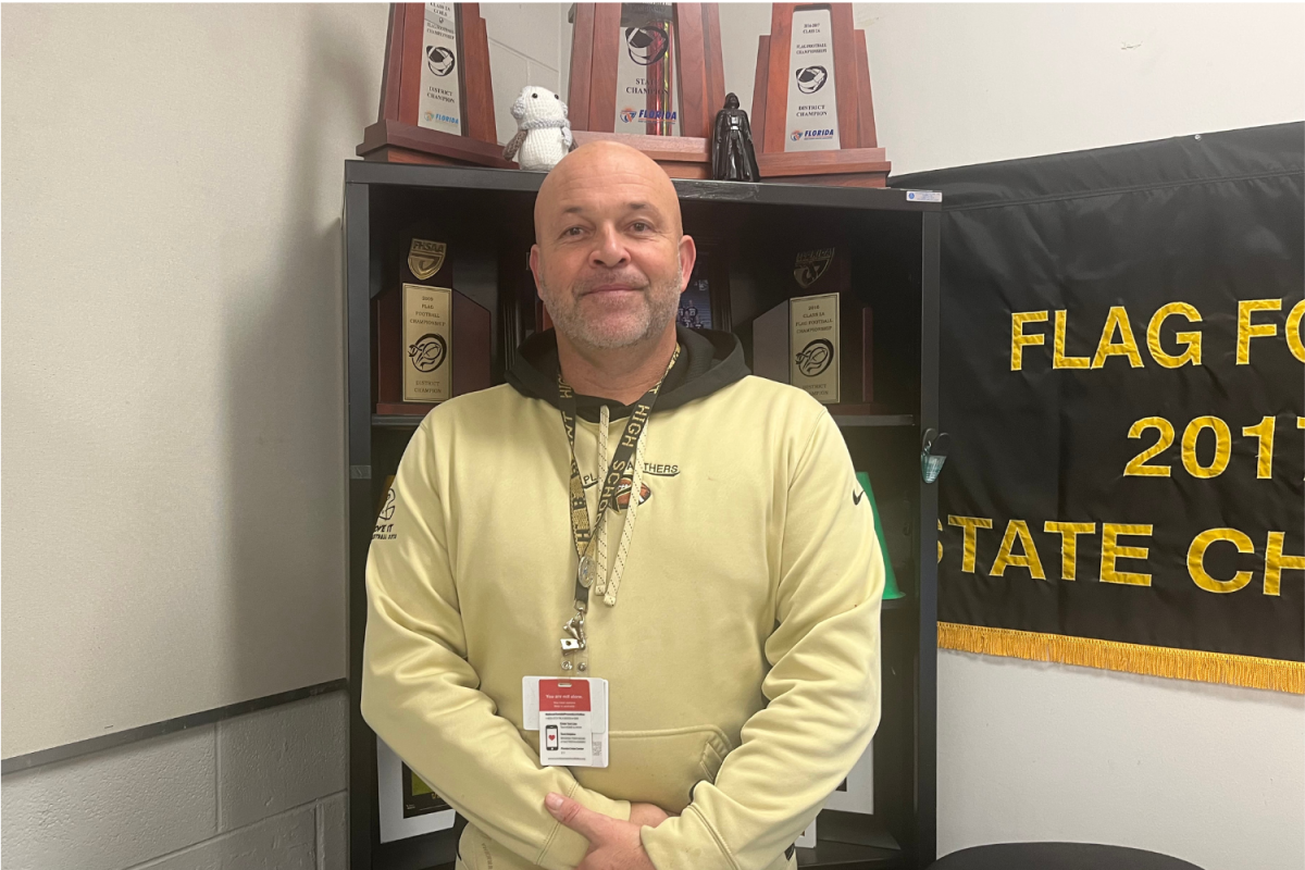 Bo Puckett stands in front of a trophy case of sports achievements. Puckett has been a coach for the Plant football, flag football, and baseball teams throughout his 25 years at Plant. 