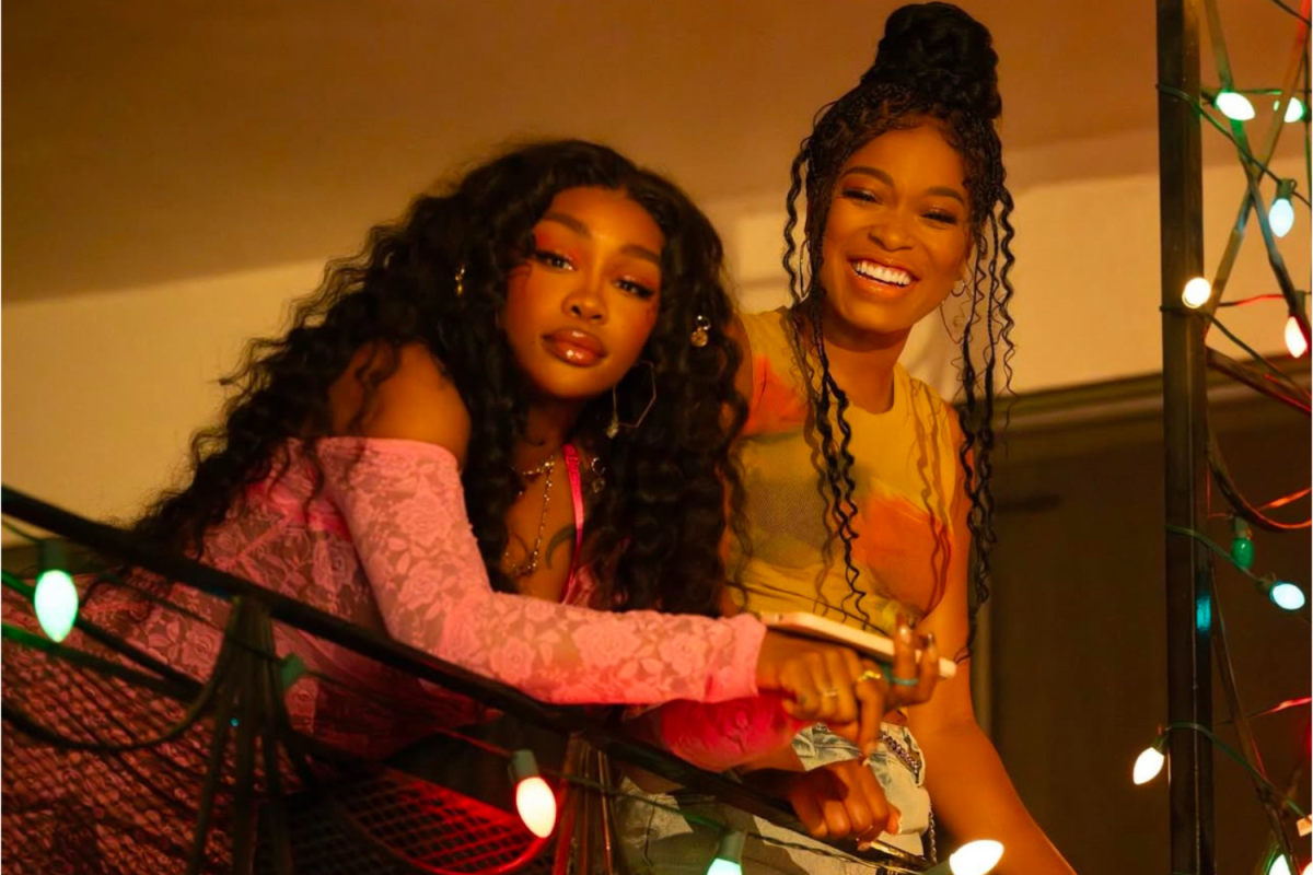 The two friends share a light moment on the balcony, their smiles reflecting hope and joy amid life's challenges. This is a tender scene from One of Them Days that highlights connection and resilience.