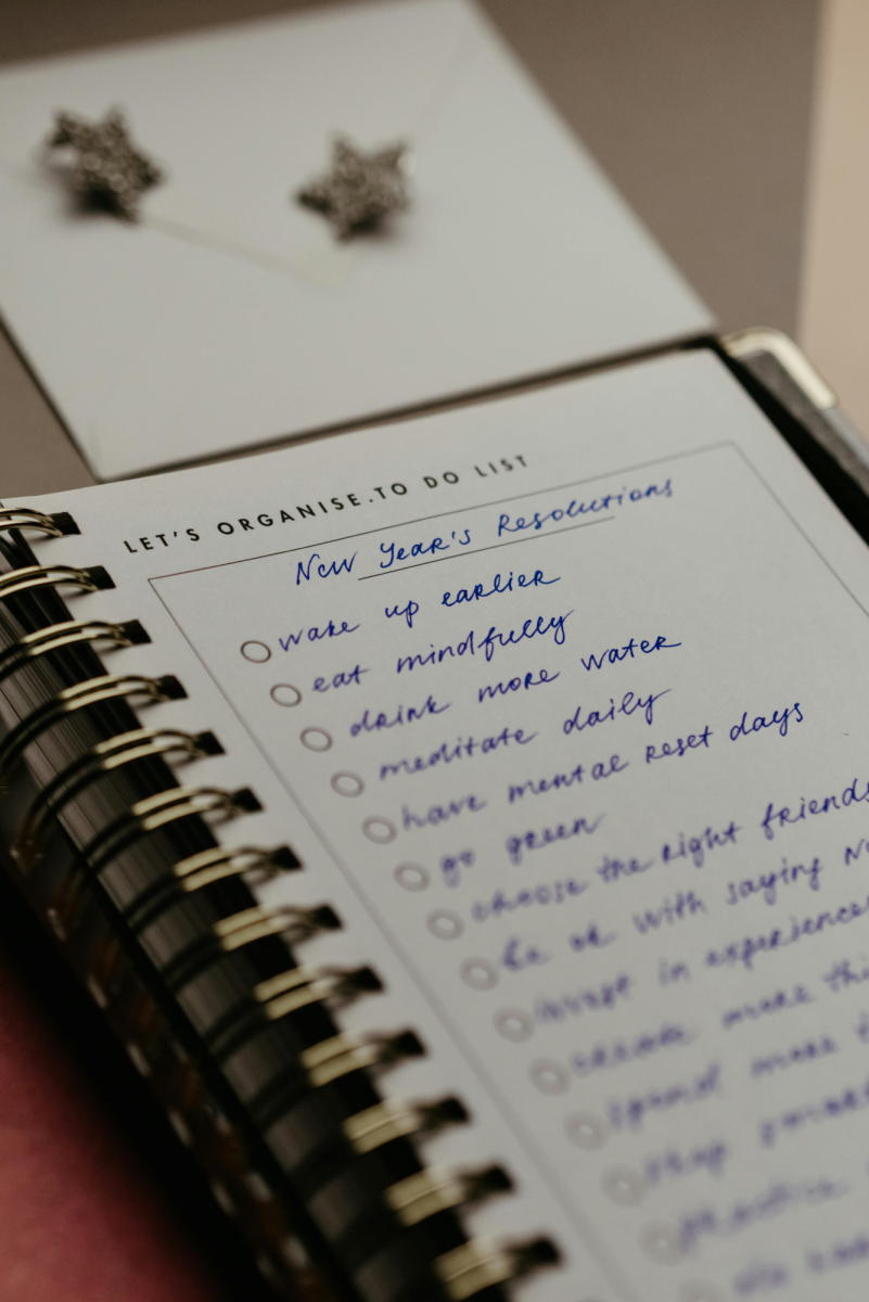 A handwritten list of New Year's resolutions sits on a notebook. Writing these goals down to start the year with a clear and organized mind.